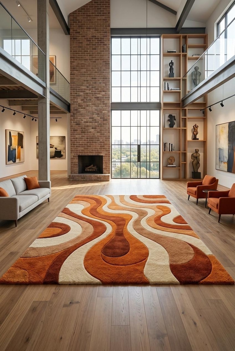 May include: A large, retro-style area rug with a wavy pattern in shades of orange, brown, and cream. The rug is the focal point of a spacious room with hardwood floors, a brick fireplace, and large windows. The room also features a sofa and armchairs.
