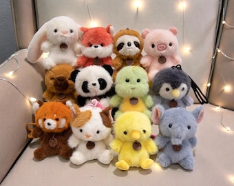 Può includere: Una collezione di peluche di animali, tra cui un coniglio bianco, una volpe rossa, un panda, un bradipo, un maiale rosa, un pinguino, un panda rosso, un gatto, una tartaruga verde, un'anatra gialla e un elefante blu. Ogni peluche ha un piccolo cartellino di legno.