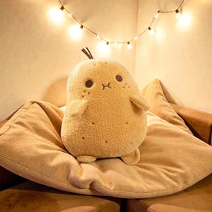 May include: A soft toy potato with a friendly face, small arms, and feet, sitting on a tan cushion. The potato is light brown with darker brown spots. A string of fairy lights hangs above, creating a warm, inviting scene.