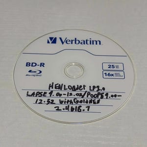 May include: A white Verbatim BD-R disc with blue text and a central hole. The disc has handwritten text including "HEN LOAdet LP2.0" and "LAPSE 4.00-12.02/POOPS9.00-". It indicates 25 GB capacity and 16x speed.