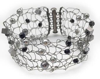 May include: A silver wire bracelet with black and silver beads. The bracelet is made of a delicate wire mesh and has a clasp closure.