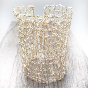 May include: A gold wire bracelet with a delicate, open-weave design. The bracelet is made of thin wire that is woven together to create a mesh-like pattern.