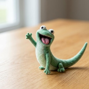Puede incluir: Figura de lagarto de fieltro verde hecha a mano, con una expresión sonriente y un brazo ondeando. El lagarto tiene ojos blancos y una lengua rosa, y está colocado sobre una superficie de madera.