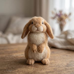 May include: A handcrafted, tan-colored felt bunny rabbit with long, floppy ears and a fluffy white chest. The bunny is standing upright on its hind legs, with its front paws held close to its chest. The rabbit is a charming, handmade decorative item.