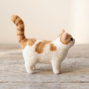 Pu&ograve; includere: Una statuetta di gatto in lana infeltrita ad ago, con corpo bianco e macchie color arancio zenzero sulla schiena e sulla testa. Il gatto ha una coda lunga e dritta, piccole orecchie a punta e occhi scuri, con una finitura in lana testurizzata.