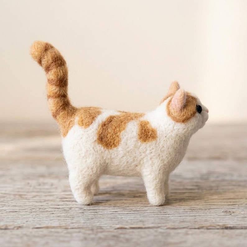 Pu&ograve; includere: Una statuetta di gatto in lana infeltrita ad ago, con corpo bianco e macchie color arancio zenzero sulla schiena e sulla testa. Il gatto ha una coda lunga e dritta, piccole orecchie a punta e occhi scuri, con una finitura in lana testurizzata.