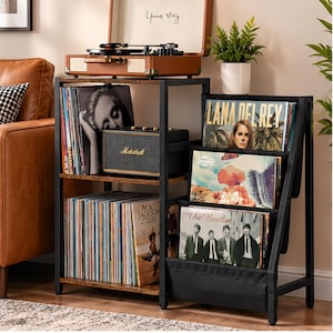 May include: A two-part vinyl record storage unit with a black metal frame and brown wood-grain shelves. The left side features two tiers for vertical record storage and a Marshall speaker. The right side has three angled fabric display slots.