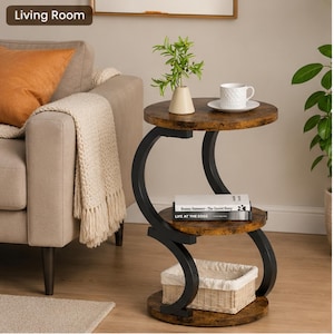 May include: A three-tier side table with a dark brown wood-grain finish and a black metal S-shaped frame. The table features three circular shelves, a small beige vase, a white mug on a saucer, two stacked books, and a woven white storage basket.