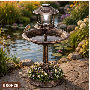 May include: A bronze-colored bird bath featuring a central pedestal, a wide basin, and a pagoda-style solar light fixture on top. A small bird is perched on the edge of the basin, and the base is surrounded by a ring of small white and purple flowers.