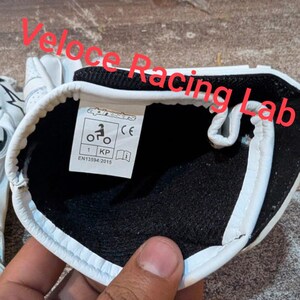 Op de afbeelding: Witte motorhandschoenen met zwarte voering en witte rand. De handschoenen hebben een label met de tekst "alpinestars" en symbolen. Ontworpen voor motorraces, ze zijn gemaakt van duurzaam materiaal.