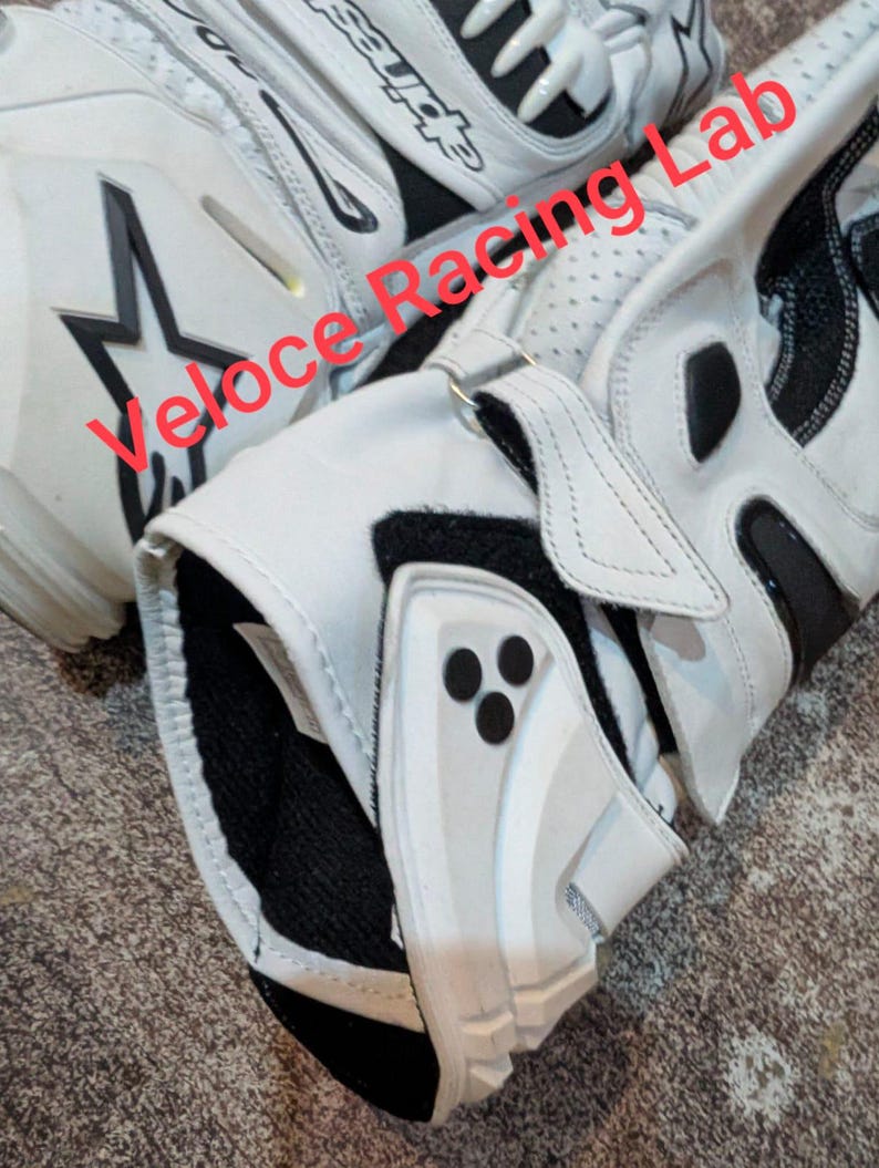 Op de afbeelding: Witte en zwarte motorhandschoenen met de tekst "Veloce Racing Lab". De handschoenen hebben een sterlogo en zwarte accenten. De handschoenen zijn gemaakt van leer en hebben een beschermend ontwerp.