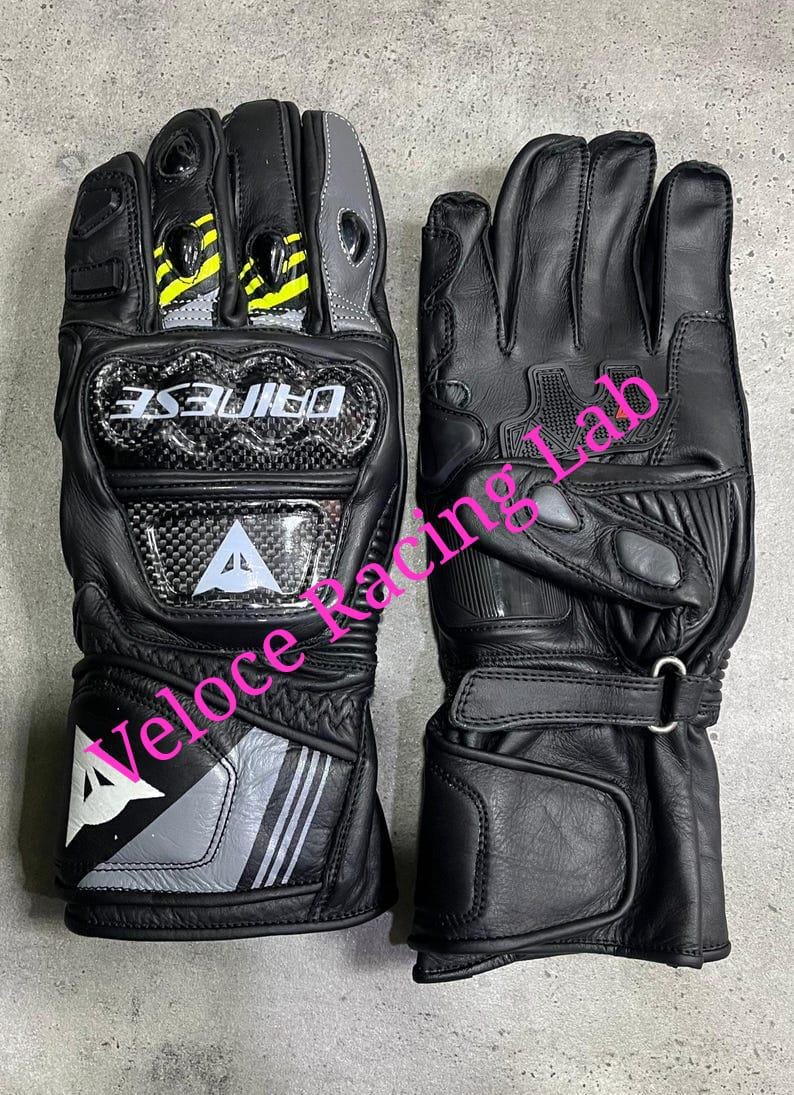 May include: Pair of black leather motorcycle gloves with carbon fiber knuckle protection. Features gray and yellow accents, the brand name "DAINESE", and the "Veloce Racing Lab" logo.