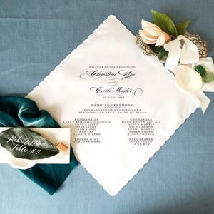 May include: White wedding ceremony program printed on a handkerchief with a scalloped edge. The program lists the names of the bride and groom, Christine Kim and Carl Master, and the wedding date, June 3, 2010. The program also lists the names of the bridesmaids and groomsmen.