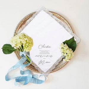 women's lace handkerchief laying flat with white florals and blue ribbon tied around the stem