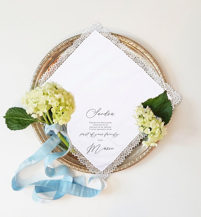 women's lace handkerchief laying flat with white florals and blue ribbon tied around the stem