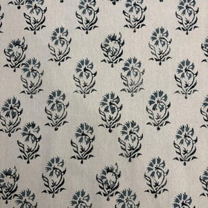 May include: Off-white fabric with a repeating pattern of stylized floral motifs. Each flower is composed of blue-gray petals and black stems and leaves. The design is evenly spaced across the fabric, creating a consistent and visually appealing texture.