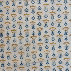 May include: Close-up of a cream-colored fabric with a repeating floral pattern. The design features stylized flowers in shades of gold and blue. The flowers are arranged in a grid-like formation, creating a visually appealing textile.