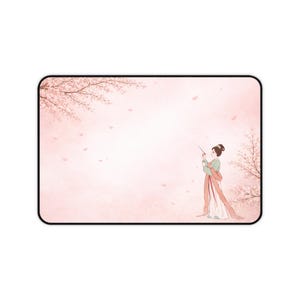 Puede incluir: Alfombrilla de ratón rectangular con un fondo rosa suave. Presenta una ilustración en acuarela de una mujer con vestimenta asiática tradicional. Ramas de cerezo en flor enmarcan la parte superior y derecha, con pétalos cayendo.