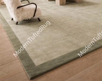 May include: A large, rectangular area rug in a neutral color palette. The rug features a light green central field with a darker green border. The text "Modern Tufted Rug" is visible on the rug. The rug is placed on a hardwood floor.