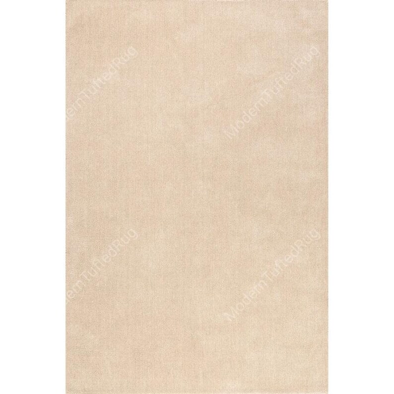 Puede incluir: Una alfombra rectangular beige con una textura suave y afelpada. La alfombra tiene un color s&oacute;lido y un dise&ntilde;o sencillo, adecuado para varios estilos de interior. La alfombra es de color neutro.