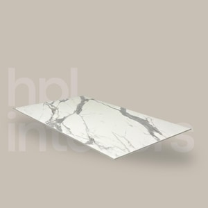 Może przedstawiać: Prostokątna biała płyta marmurowa z szarym żyłkowaniem. Płyta jest ustawiona pod kątem, prezentując swoją polerowaną powierzchnię i naturalny wzór kamienia. Tło jest jednolite i neutralne.