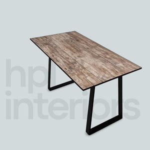 Könnte beinhalten: Ein rechteckiger Tisch mit einer verwitterten, braunen Holzmaserung und einem schwarzen Metallrahmen mit zwei U-förmigen Beinen. Der Text hp interiors ist im Hintergrund sichtbar. Der Tisch hat eine flache Platte und ein stabiles, kantiges Gestell.