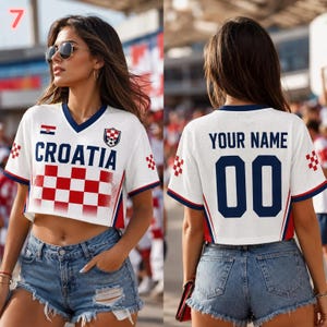 May include: A white cropped V-neck jersey featuring the text CROATIA and a red and white checkered pattern on the front. The back displays the text YOUR NAME and the number 00 in dark blue. The jersey has short sleeves with red and blue trim.