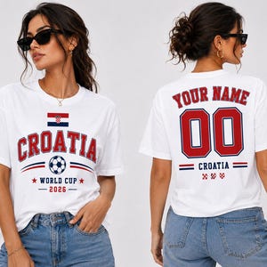 Op de afbeelding: Wit T-shirt met "CROATIA" in rode letters, een voetbal en de Kroatische vlag. Het ontwerp aan de voorkant bevat "WORLD CUP 2026". De achterkant toont "YOUR NAME" en het nummer "00" in rood.