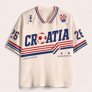 Pu&ograve; includere: Una maglia a scollo a V color crema con una trama a rete. La parte anteriore presenta la scritta CROATIA con un pallone da calcio al posto della lettera O, il numero 26 sulle maniche, un'icona a forma di trofeo, lo stemma croato e il testo CROATIA SOCCER VATRENI MATCH 26.
