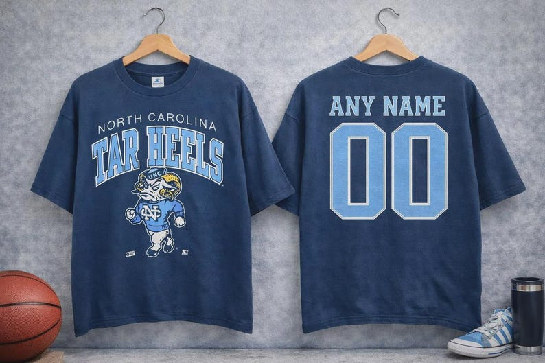 May include: Navy blue t-shirt featuring "North Carolina Tar Heels" text and a ram mascot graphic on the front. The back displays "ANY NAME" and the number "00" in light blue.