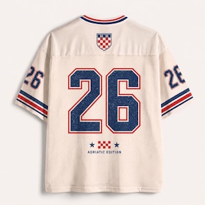 Pu&ograve; includere: Una maglia in mesh color bianco sporco con il numero 26 in grandi cifre blu con bordi rossi sul retro. Il design include uno stemma a scacchi rosso e bianco, strisce blu e rosse sulle maniche e la scritta ADRIATIC EDITION con due stelle.