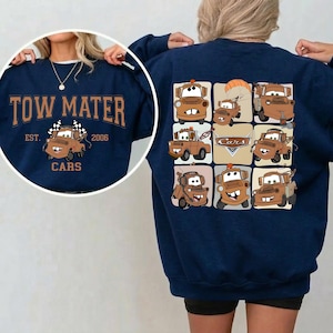 Op de afbeelding: Marineblauwe sweatshirt met een cartoonafbeelding van Takel uit de film Cars. De voorkant toont "TOW MATER" boven Takel met "EST. 2006 CARS". De achterkant heeft een raster van Takel-afbeeldingen. Een leuke, casual top voor fans van de animatiefilm.