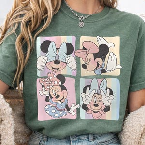 May include: Green t-shirt featuring four squares with different Minnie Mouse poses. Each square has a pastel rainbow striped background. Minnie is wearing different bows and outfits in each square.
