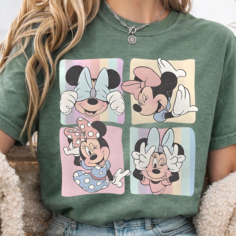 May include: Green t-shirt featuring four squares with different Minnie Mouse poses. Each square has a pastel rainbow striped background. Minnie is wearing different bows and outfits in each square.