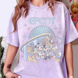 Może przedstawiać: Jasnofioletowa koszulka z napisem "EPCOT" nad grafiką sfery Spaceship Earth i postaciami Disneya: Miki, Minnie, Donald, Goofy i Pluto. Projekt zawiera gwiazdy i futurystyczny monorail.