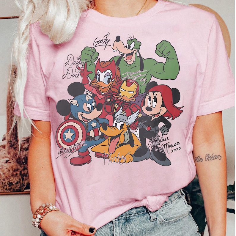 Puede incluir: Camiseta rosa claro con un dise&ntilde;o de personajes de Disney como superh&eacute;roes. Mickey Mouse es el Capit&aacute;n Am&eacute;rica, Minnie Mouse es Viuda Negra y Goofy tambi&eacute;n aparece. El texto incluye "Mickey Mouse".