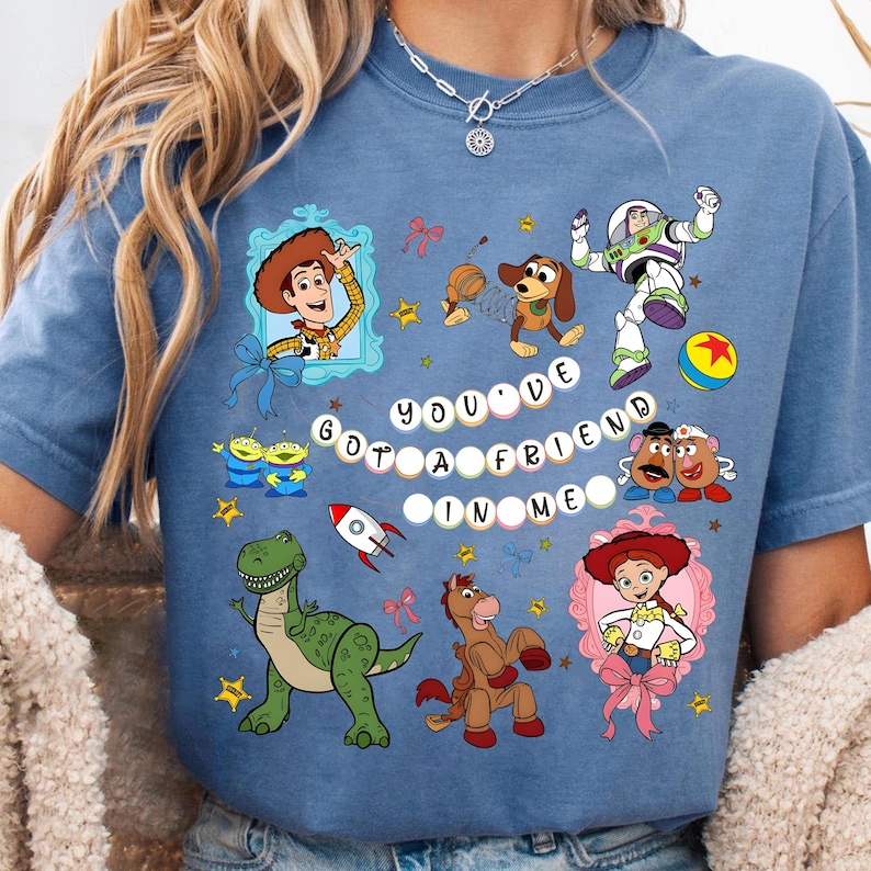 May include: A blue t-shirt featuring various Toy Story characters, including Woody, Buzz Lightyear, and Jessie. The phrase "You've Got a Friend in Me" is displayed in white letters. The design includes stars, bows, and a rocket.
