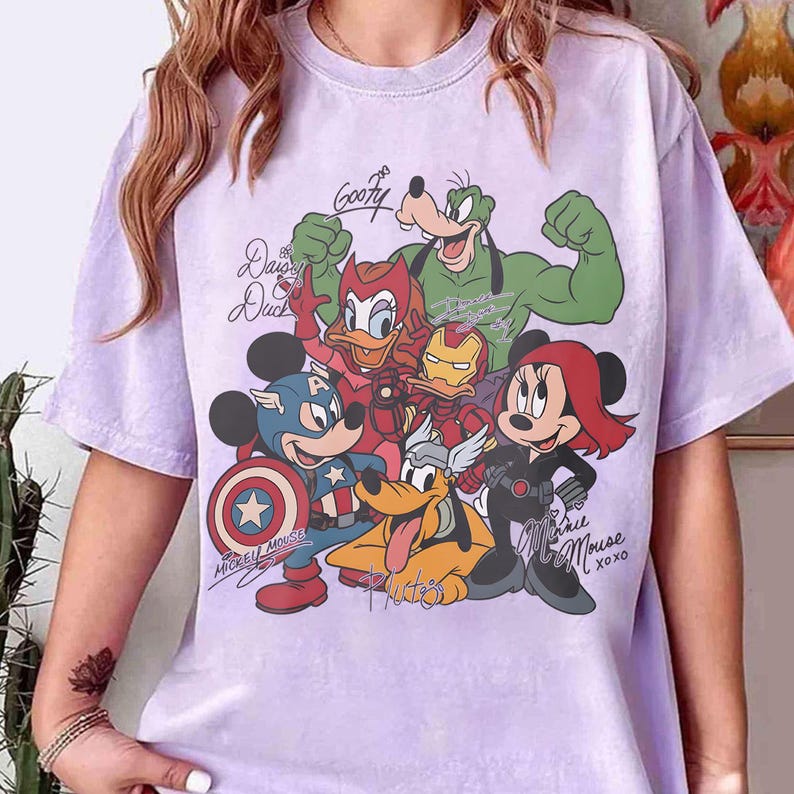 Puede incluir: Camiseta lila claro con un gr&aacute;fico de personajes de Disney con disfraces de superh&eacute;roes. El dise&ntilde;o incluye Mickey Mouse, Minnie Mouse, Goofy, Donald Duck y Pluto. El texto incluye "Goofy", "Daisy Duck", "Mickey Mouse XOXO".