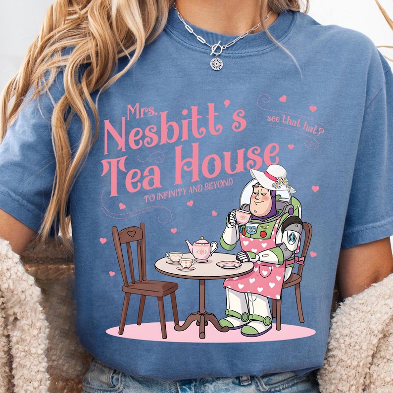 May include: Blue t-shirt featuring a cartoon illustration of Buzz Lightyear in a pink apron, white hat, and holding a teacup. The text "Mrs. Nesbitt's Tea House" is above the illustration, with "To Infinity and Beyond" below.