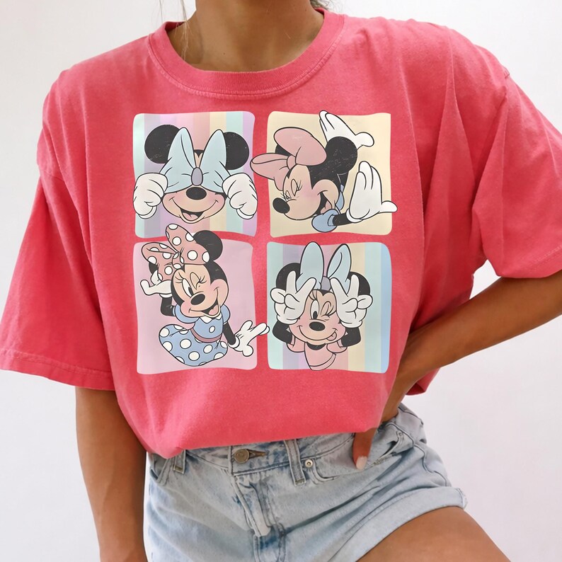 May include: A coral-colored t-shirt featuring a four-panel design of Minnie Mouse. Each panel showcases a different pose of Minnie, with colorful pastel backgrounds. Minnie is wearing bows and dresses in various colors.