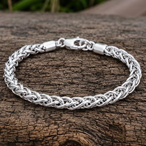 May include: A silver-toned wheat chain bracelet featuring a polished metallic finish and a secure lobster claw clasp. The bracelet is constructed from interconnected, braided metal links that form a continuous, rounded, and flexible circular band.