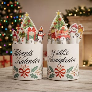 May include: Two cylindrical white containers featuring festive holiday graphics, including holly leaves, red bows, and numbered cutouts of Christmas trees, gifts, a penguin, a car, and a bear. The text reads Advents Kalender and 24 süße Kleinigkeiten.