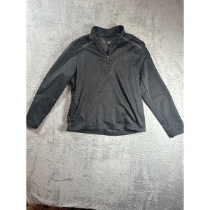 May include: A charcoal gray long-sleeve pullover with a quarter-zip closure. The top features a mock neck collar and the Callaway logo on the chest. The shoulders have a darker gray accent.