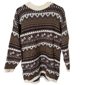 May include: A long-sleeved sweater with a cream-colored crew neck and cuffs. The sweater features a repeating pattern of brown, gray, white, and burgundy geometric shapes and floral motifs. The sweater is made of a soft, knitted material.