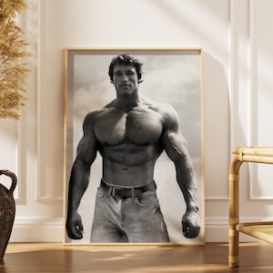 May include: Black and white framed print of a muscular person in denim jeans and a belt. The person is standing with arms at their sides, showcasing a physique. The background is a cloudy sky.