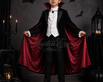 May include: A black velvet cape with a deep red satin lining and a high collar, worn over a white ruffled shirt, a white vest with buttons, and black trousers. The ensemble includes a small red gemstone pendant at the neck and black shoes.