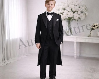 May include: A young person in a formal black tuxedo, including a long tailcoat, vest, and trousers. The outfit is completed with a white dress shirt, black bow tie, and black dress shoes. The background is a bright room with white curtains and a table with flowers.