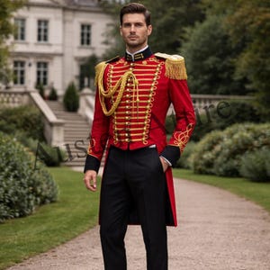 Op de afbeelding: Een rode jas in militaire stijl met gouden details, epauletten en decoratief touw. De jas wordt gecombineerd met een zwarte broek. De outfit is formeel en elegant, geschikt voor een speciale gelegenheid.