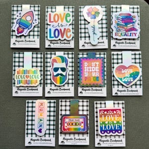 May include: A collection of magnetic bookmarks with various designs and text. The bookmarks feature colorful illustrations including a rocket, flowers, books, and the phrases "Love is Love", "Equality", and "Don't Hide Your Pride".