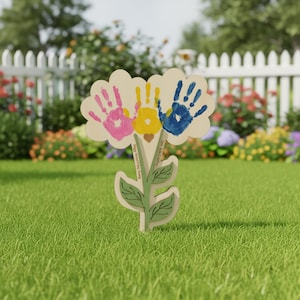 Può includere: Un paletto da giardino a forma di fiore in legno con tre impronte di mani colorate in rosa, giallo e blu. Il paletto ha uno stelo e foglie verdi, con il testo "Papa I love you" e "Love Alla & Ratha".